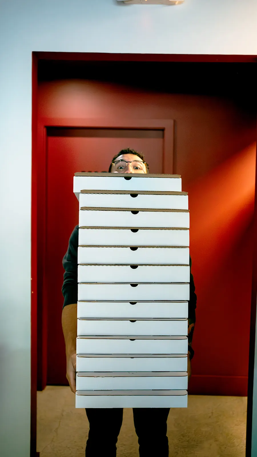 A staff member carrying a tall stack of takeout pizza boxes
