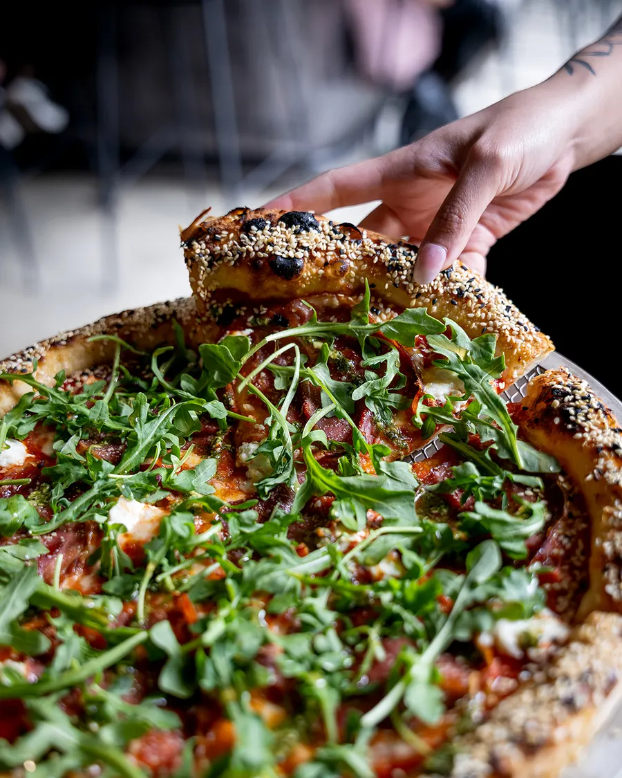 Serving a slice of The Mama with arugula and honey sesame crust
