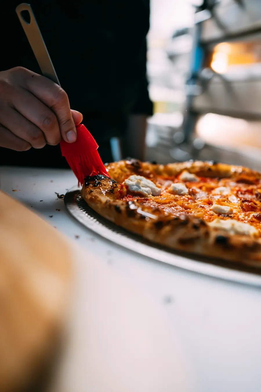 Brushing honey sesame crust on a pizza fresh out of the deck oven